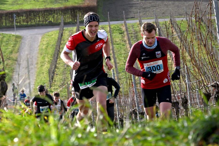 Zwei Läufer vom ASC Konstanz laufen beim Reichenauer Crosslauf zwischen den Weinstöcken auf die Hochwart. Am Sonntag, 10.12.2023.