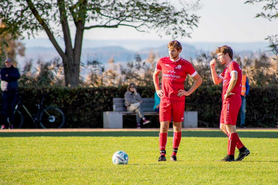 Die beiden Mittelfeldspieler Aron und Magnus stehen beim Freistoß und besprechen sich. Der Fussball liegt vor ihnen. Sie spielen in der ersten Mannschaft der SG Reichenau-Waldsiedlung in der Fussball Bezirksliga Bodensee in der Saison 2025/2026